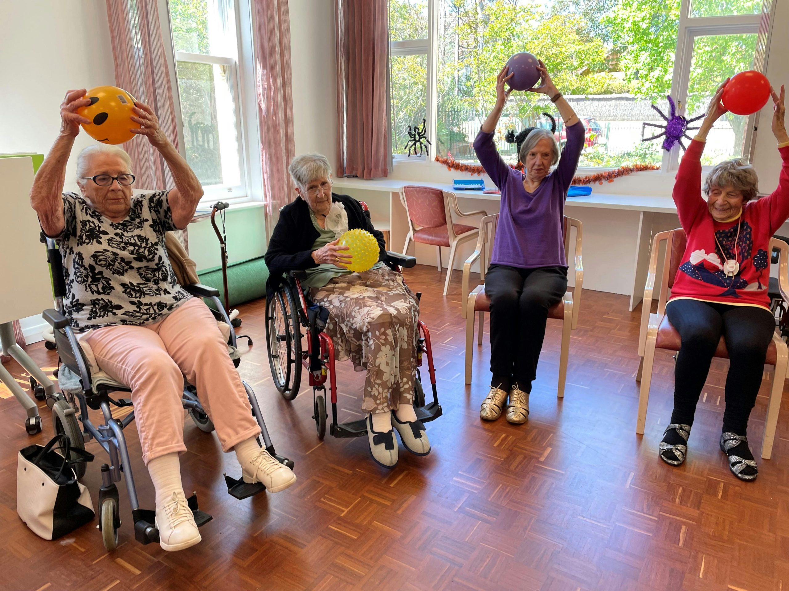 Four elderly people doing exercises from chairs with a ball 