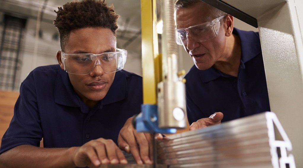 Student pushing metal through bandsaw while observed by an instructor