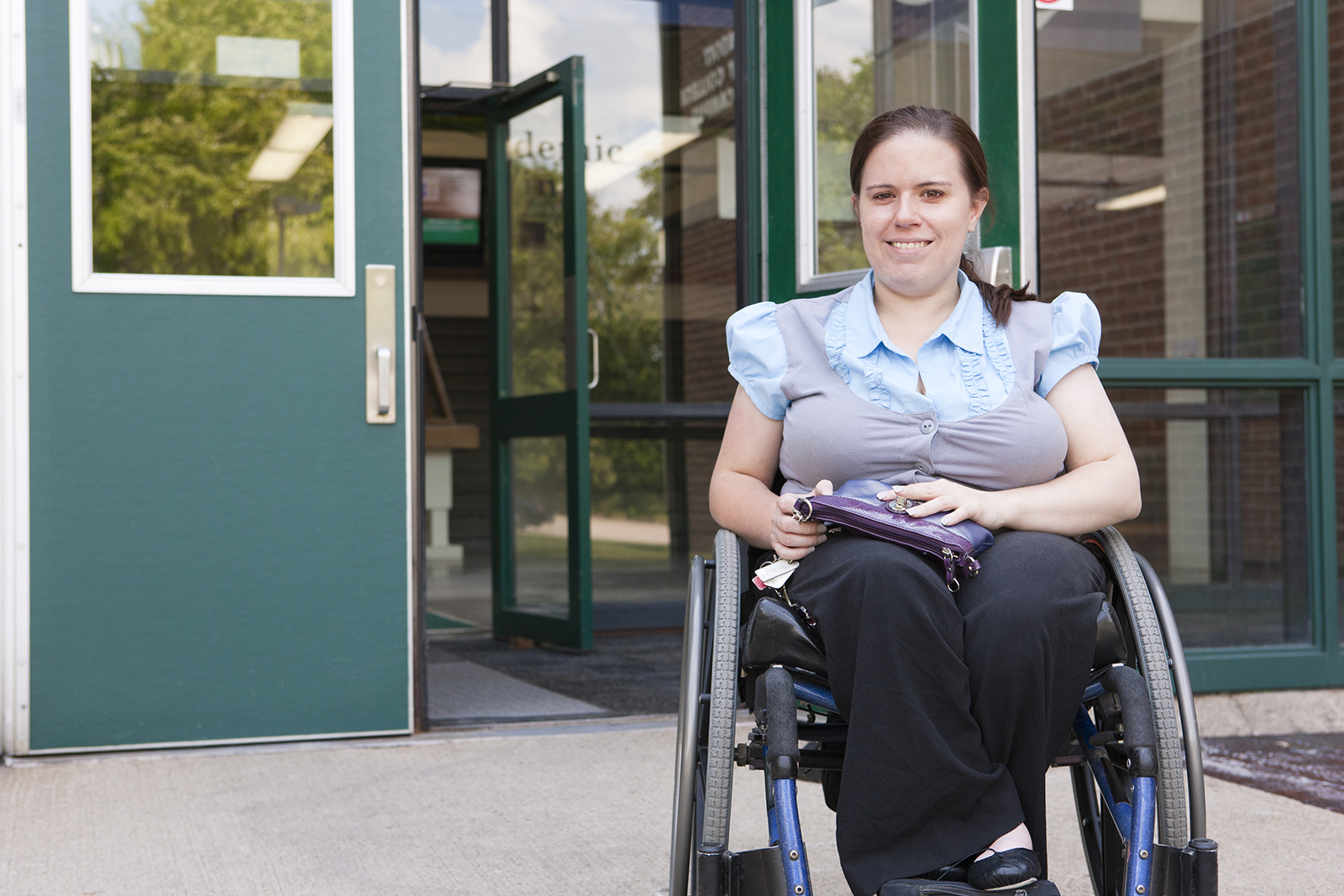 A woman in a wheelchair smiles outside of an office building