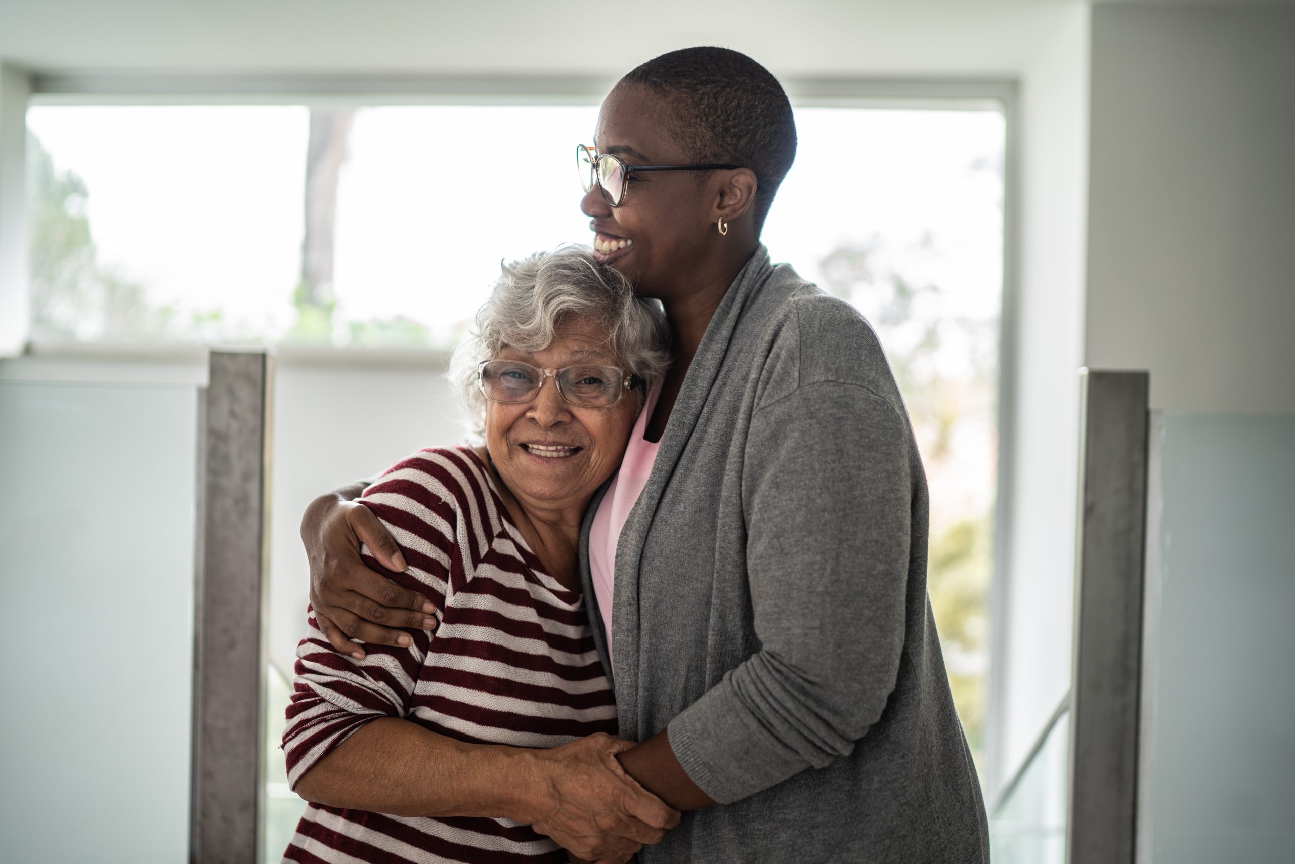 A granddaughter hugs her grandmother. They're both smiling.