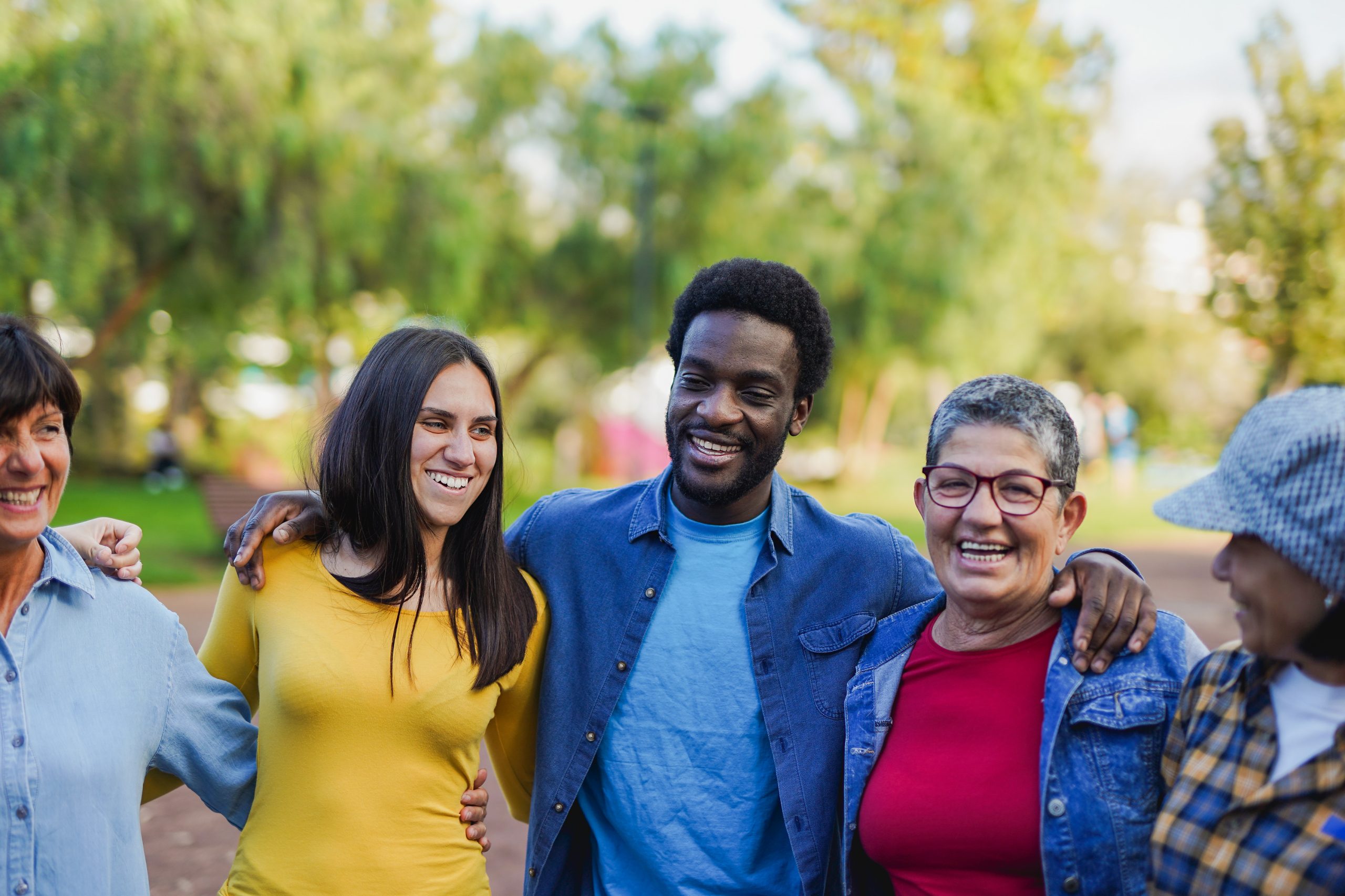 A diverse group of people of all ages and races have their arms around each other's shoulders and laugh