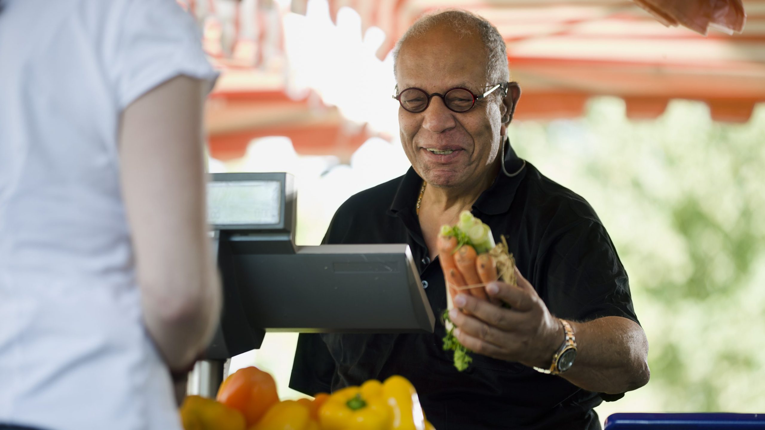 A farmer is holding carrots and selling them at a local farmers market