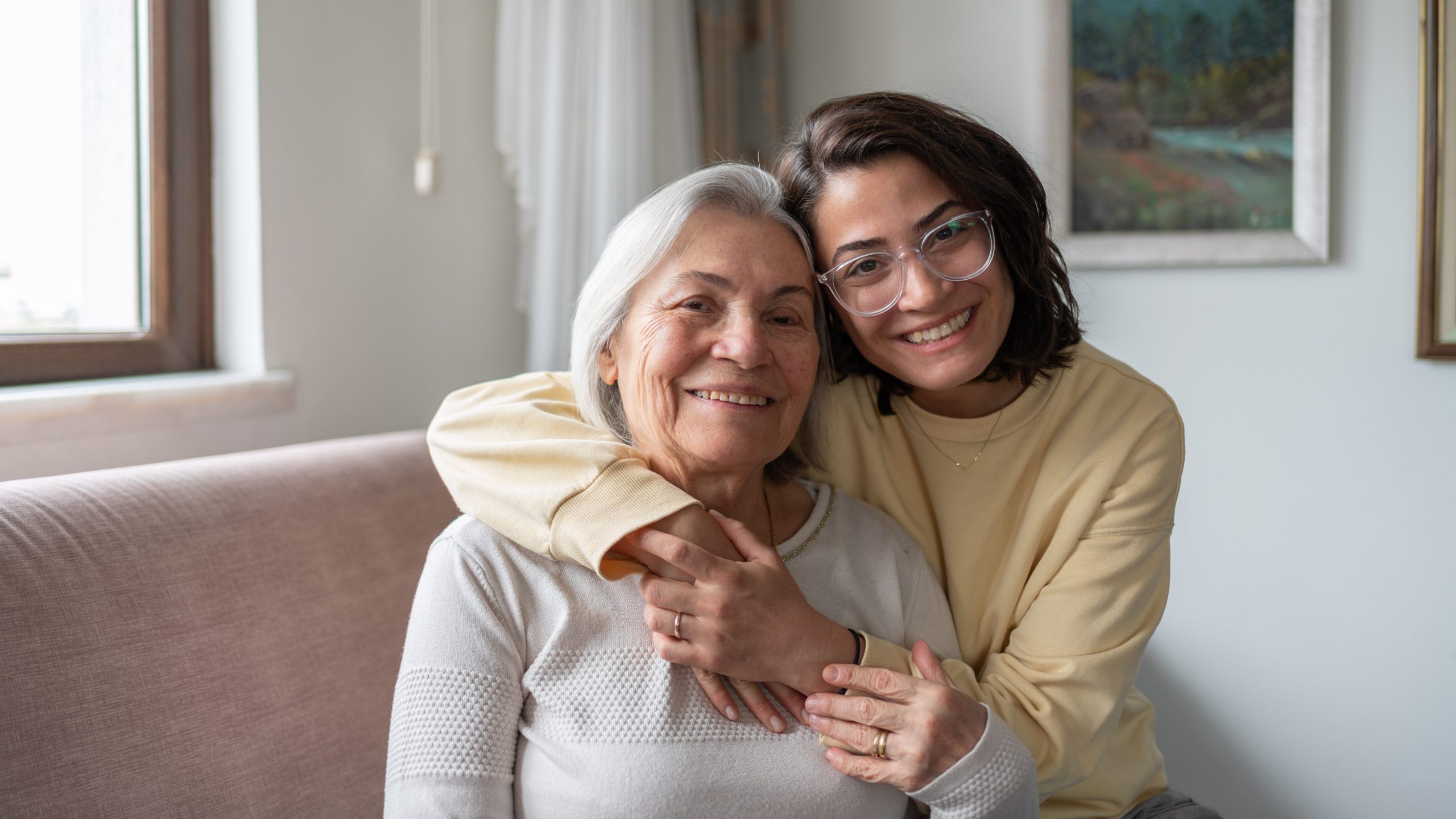 Daughter Hugging Senior Mother and smiling at camera