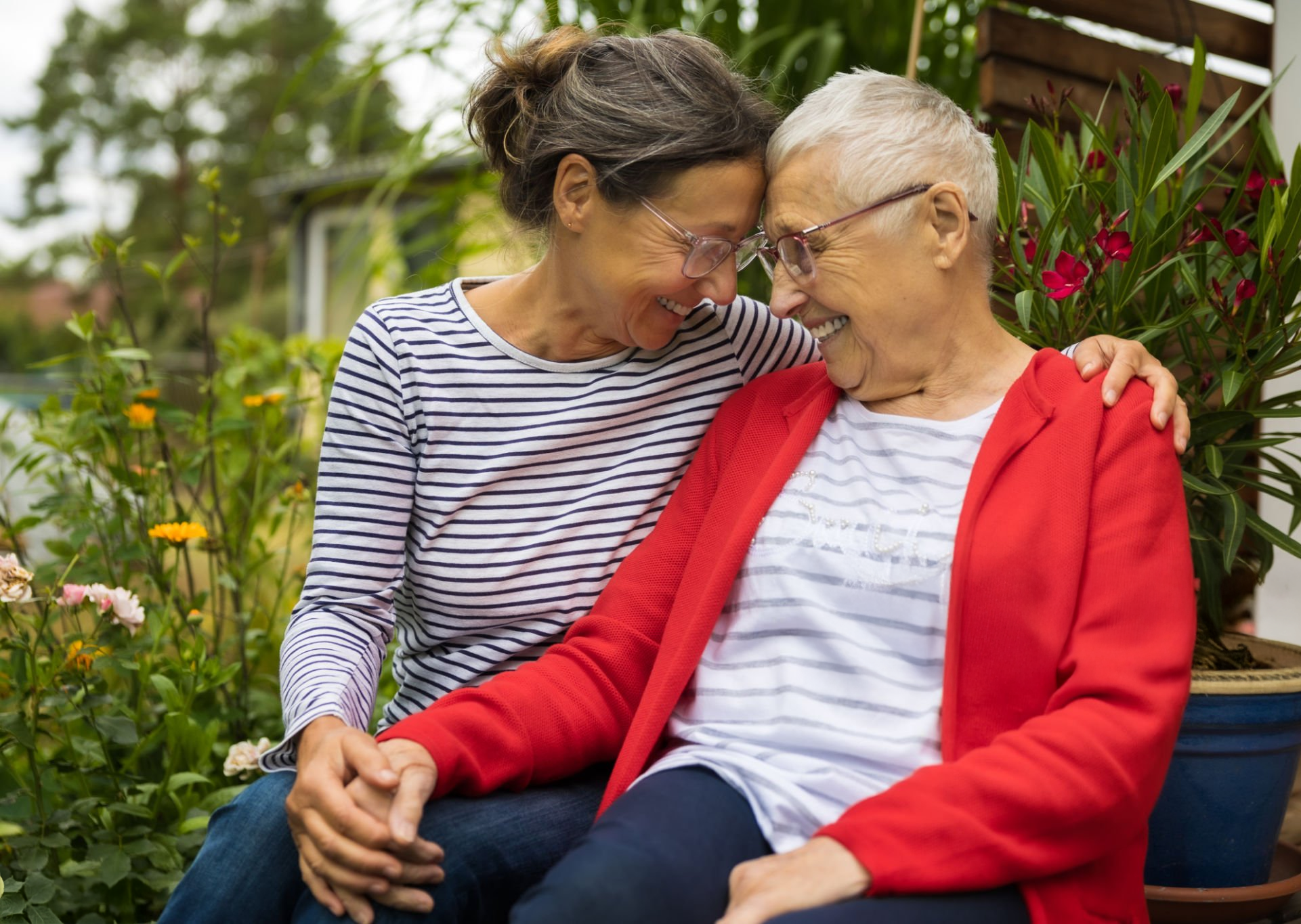 An elderly woman and her daughter embrace and smile at one another