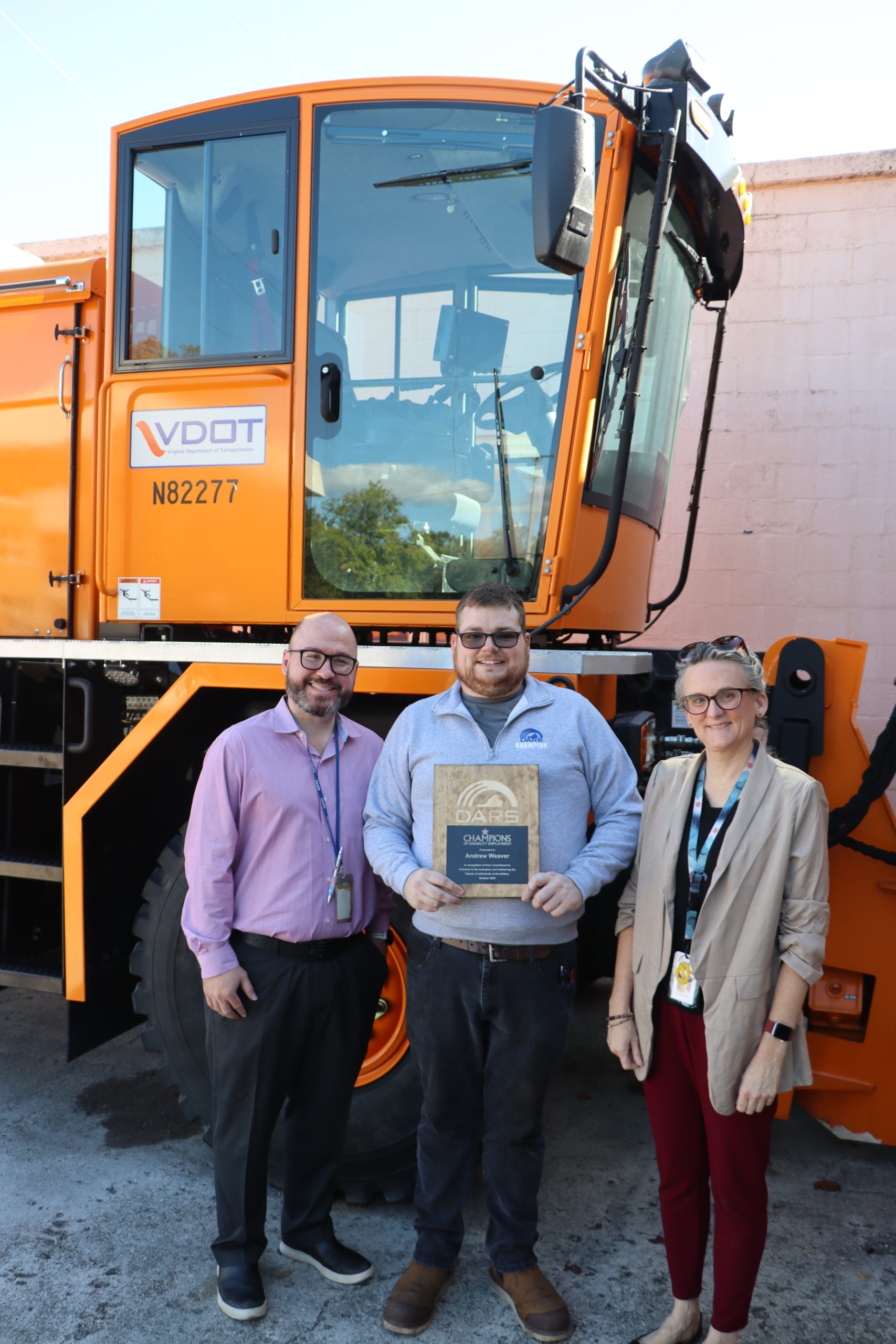photo of Andrew Weaver, holding the DARS champions of disability employment wooden plaque and standing in front of a VDOT truck. To his left and right are DARS Lynchburg office staff.